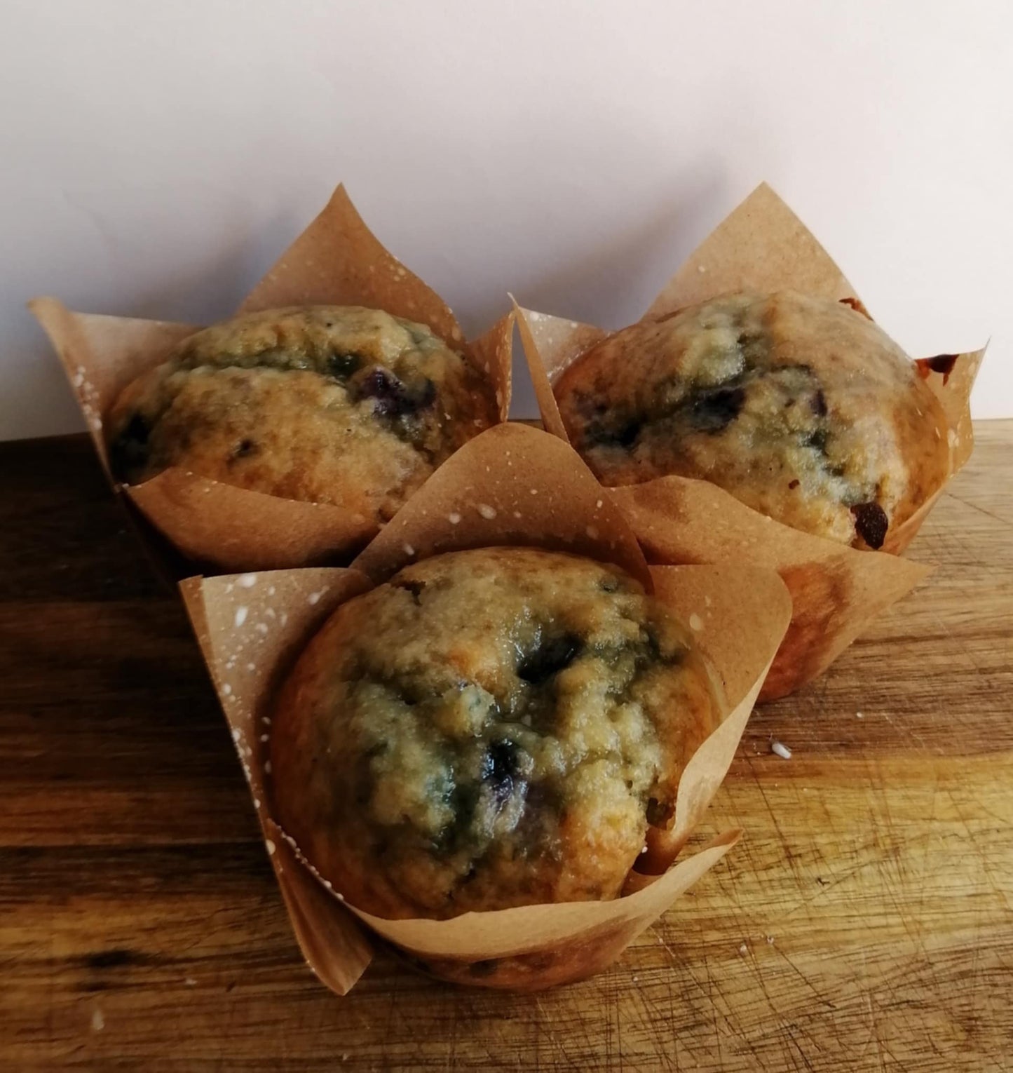 Three Lemon & Blueberry Muffins with a lemon glaze on a wooden board